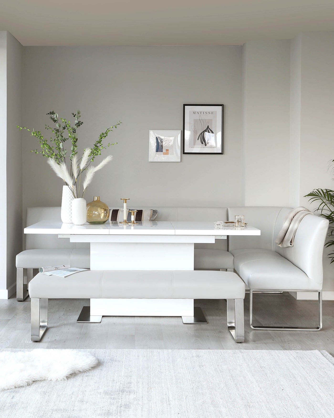 Modern dining set featuring a glossy white rectangular table with polished chrome legs, paired with a matching white leather upholstered bench on one side and a luxurious white leather dining chair with a uniquely curved backrest and chrome frame on the other. A fluffy white rug lies beneath.