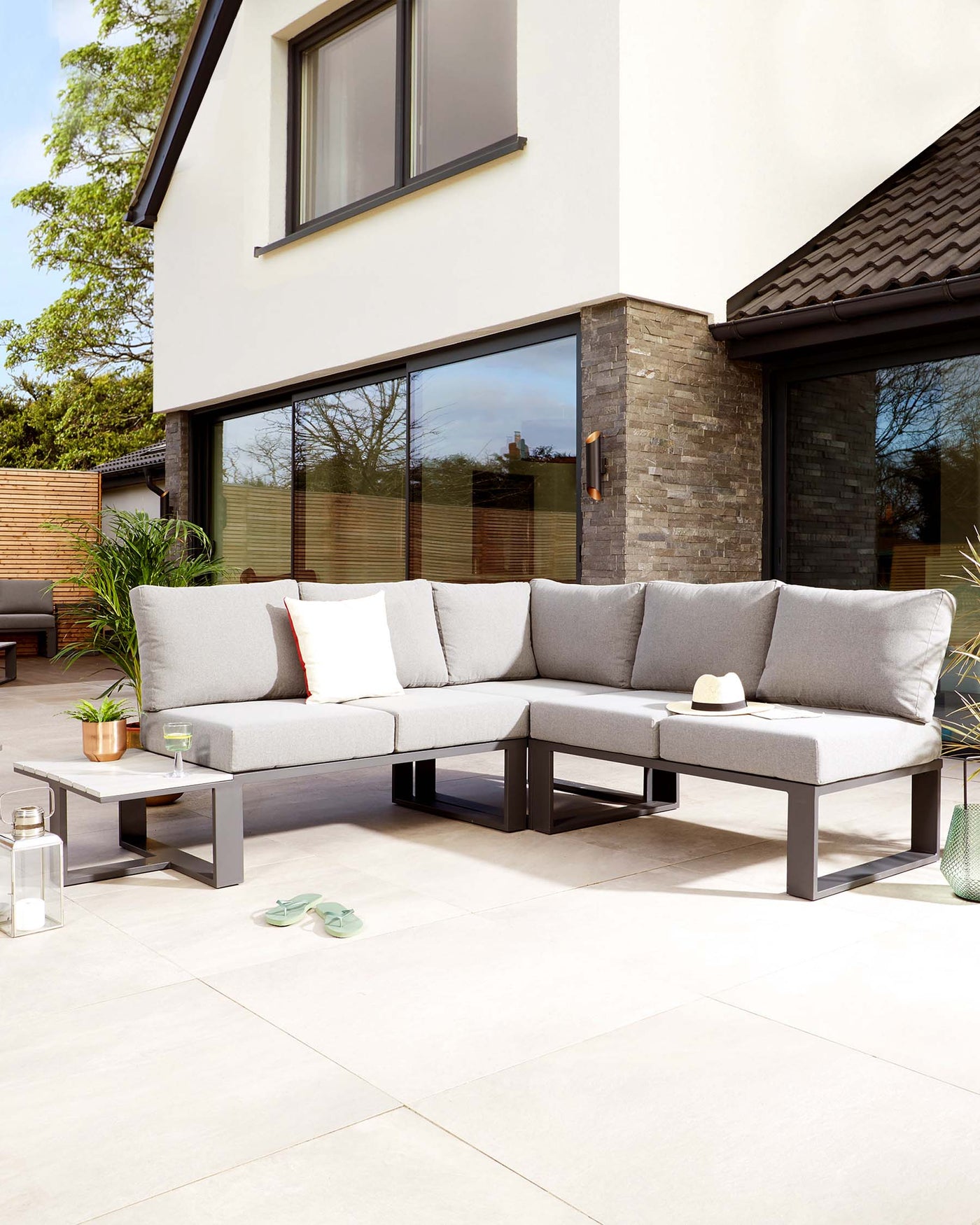 Modern outdoor L-shaped sectional sofa with light grey cushions on a minimalist dark frame, paired with a rectangular, low profile coffee table in a matching colour scheme.