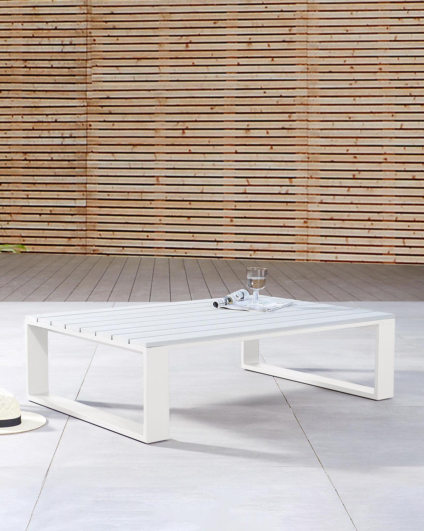 Modern outdoor white rectangular coffee table with a minimalistic design, featuring clean lines and a slatted top, set on a patio with a wooden slat background.
