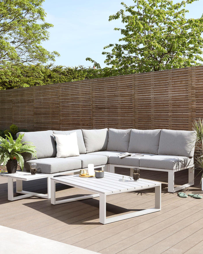Outdoor patio furniture set featuring a corner sectional sofa with grey cushions and a rectangular white coffee table with a slatted top design.