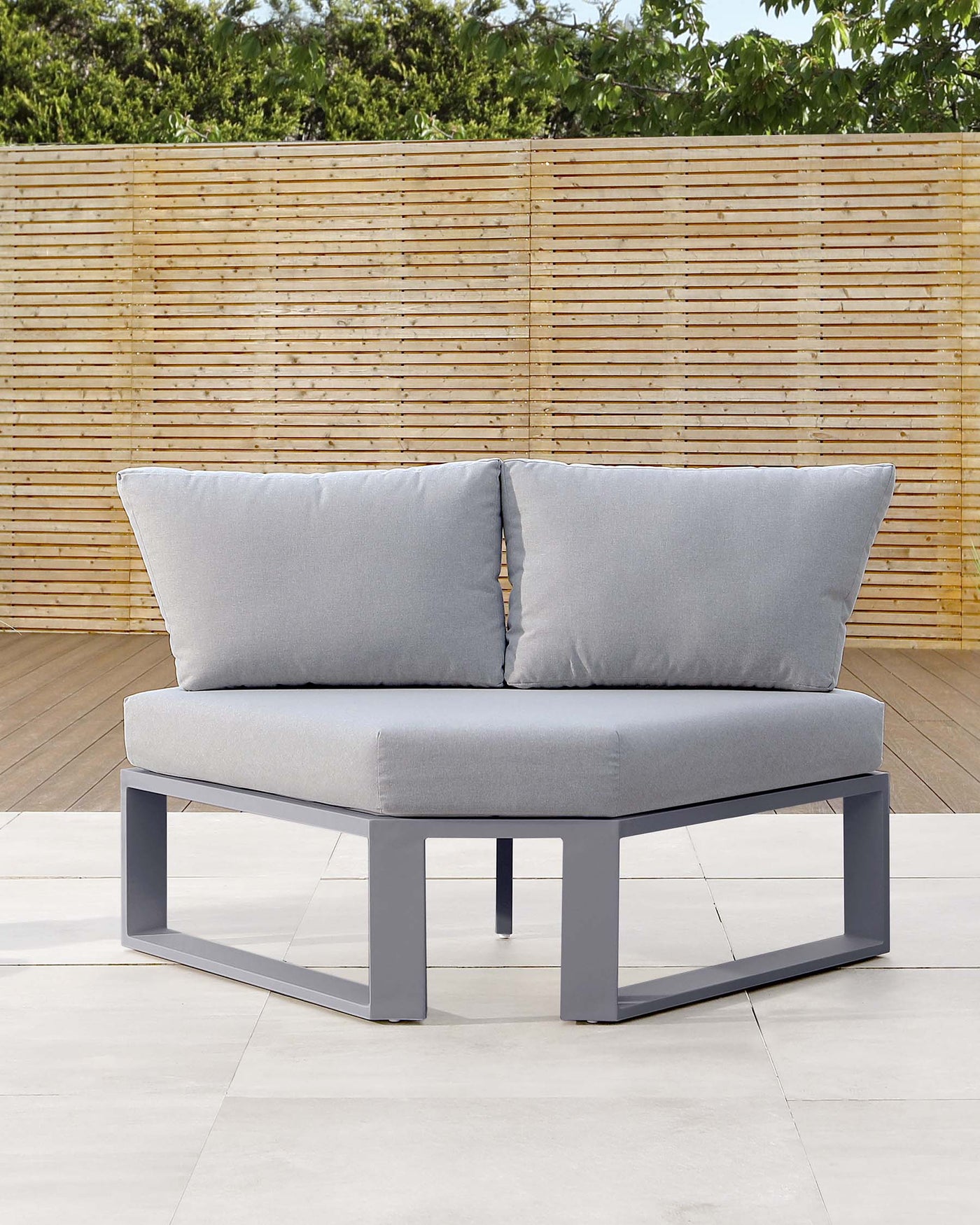 Modern outdoor loveseat with a sleek, grey metal frame and light grey cushions, featuring simple, clean lines and including two matching accent pillows, set against a natural bamboo fence backdrop.