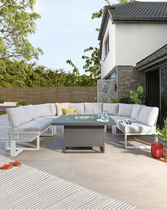 Modern outdoor furniture set featuring a sectional sofa with white cushions and a minimalist, square coffee table with a grey top and white frame, arranged on a patio area with decorative pillows and accessories.