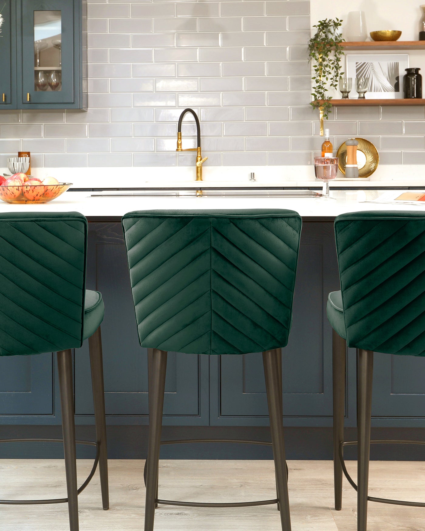 Elegant modern bar stools with plush emerald-green velvet upholstery and a distinctive geometric channel tufting on the backrest. Each stool stands on slender black metal legs with a circular footrest.