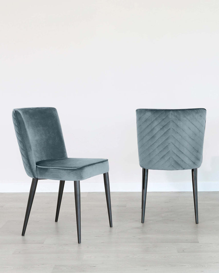 Two modern velvet dining chairs with black metal legs, one with a smooth seat and curved backrest, and the other with a chevron-patterned backrest, on a light wooden floor against a white wall.