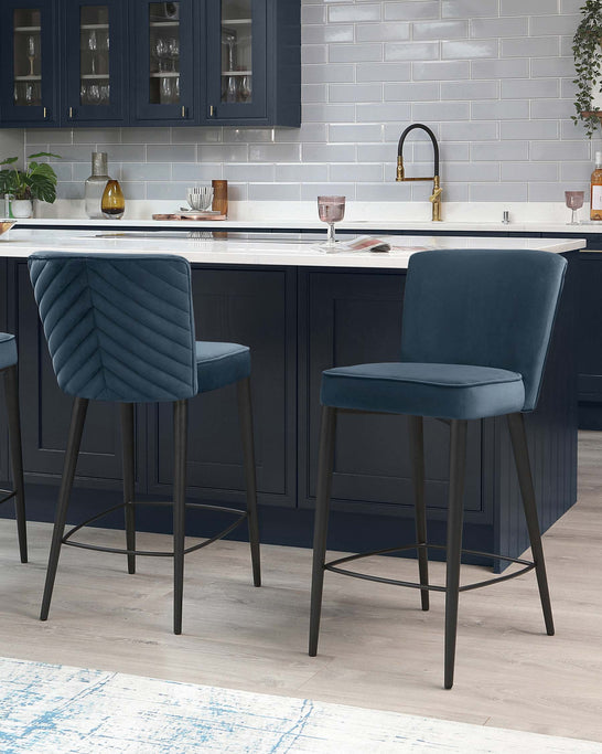 Modern kitchen with two teal blue velvet bar stools featuring quilted stitching on the backrest and sleek black metal legs with footrests.