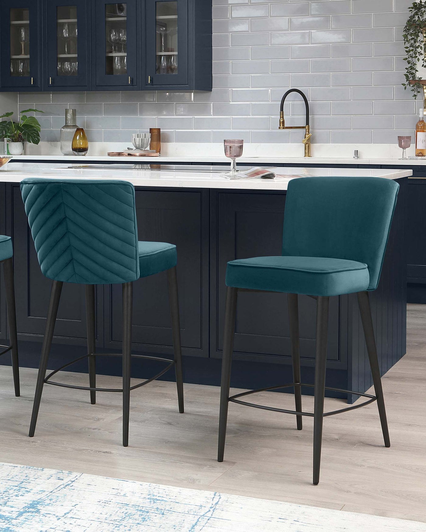 Two elegant teal blue bar stools with quilted velvet upholstery and sleek metallic legs placed against a modern kitchen island.