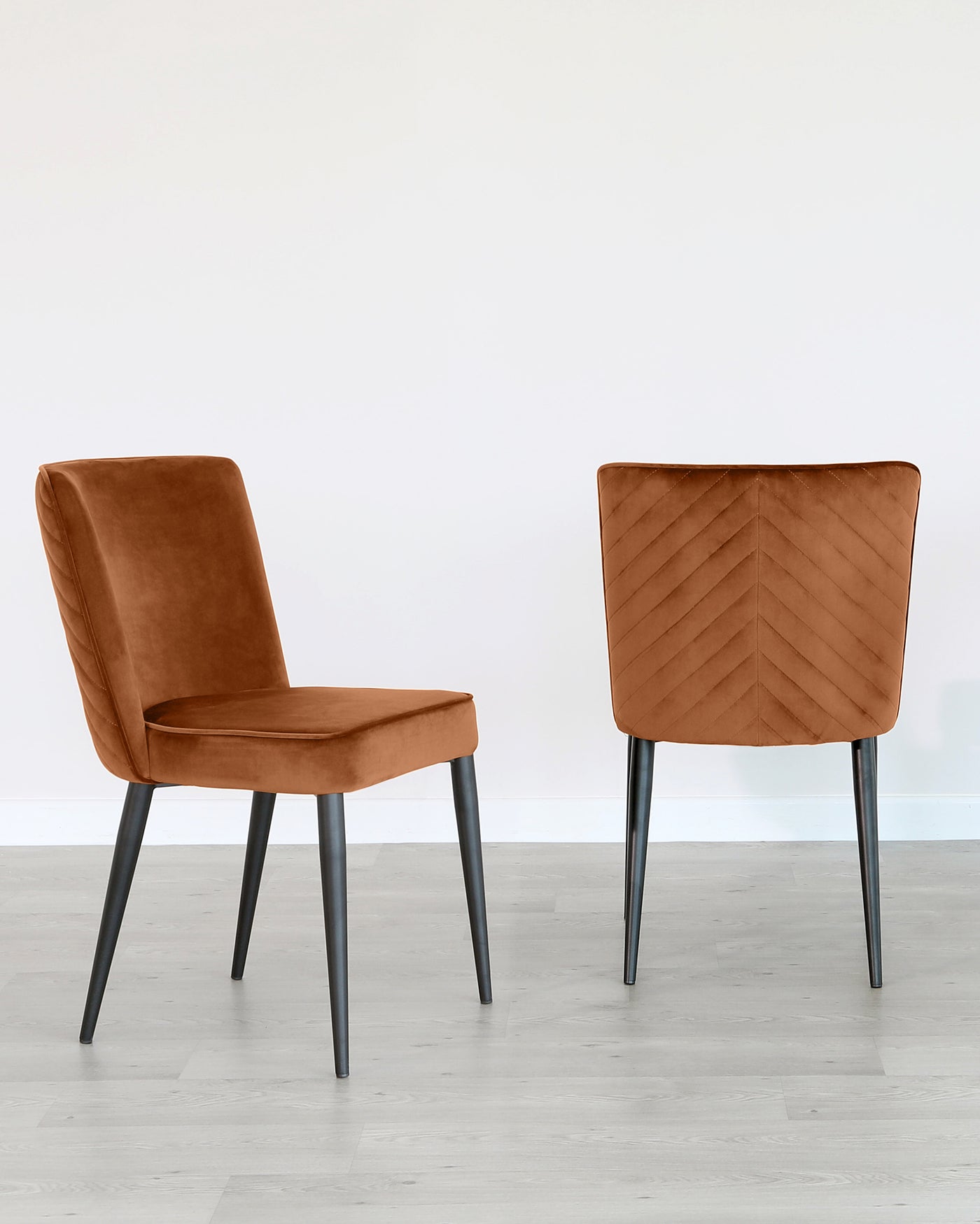 Two modern dining chairs with a sleek design, featuring caramel-coloured upholstery and dark grey metal legs. The chair in the foreground is shown from the front, while the other is viewed from the back, displaying a distinctive chevron stitching pattern.