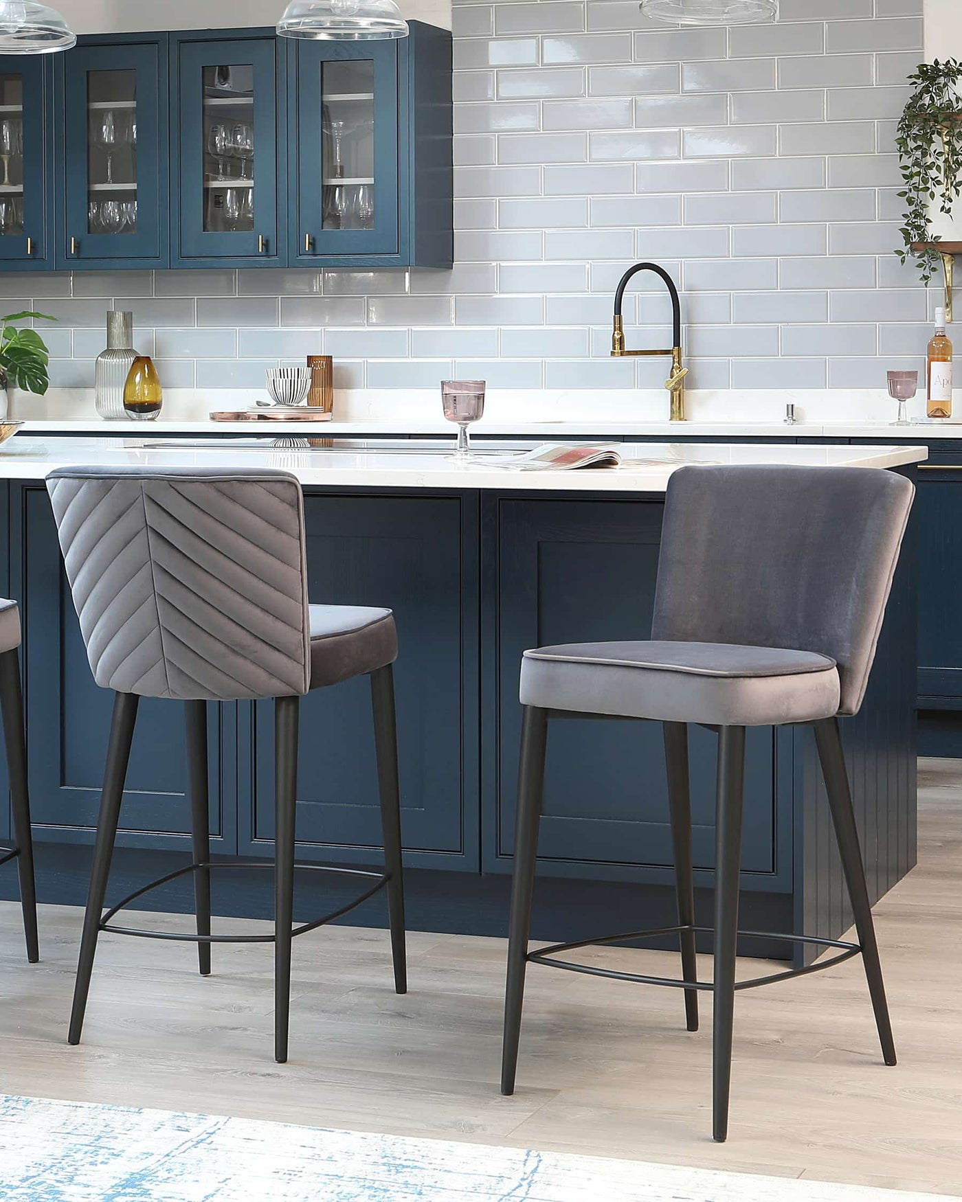 Two contemporary grey upholstered bar stools with channel tufting on the backrest, complemented by sleek black metal legs and footrests.