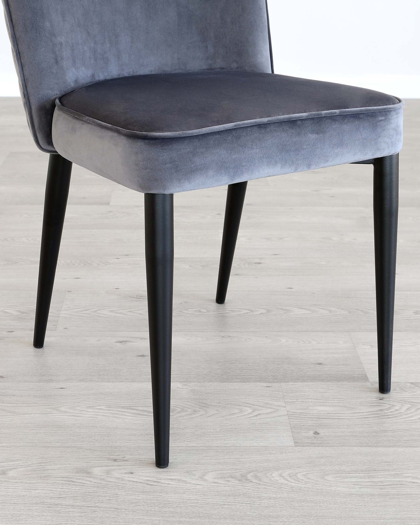 Elegant modern dining chair with a soft grey velvet upholstery and sleek black tapered legs on a light wooden floor.