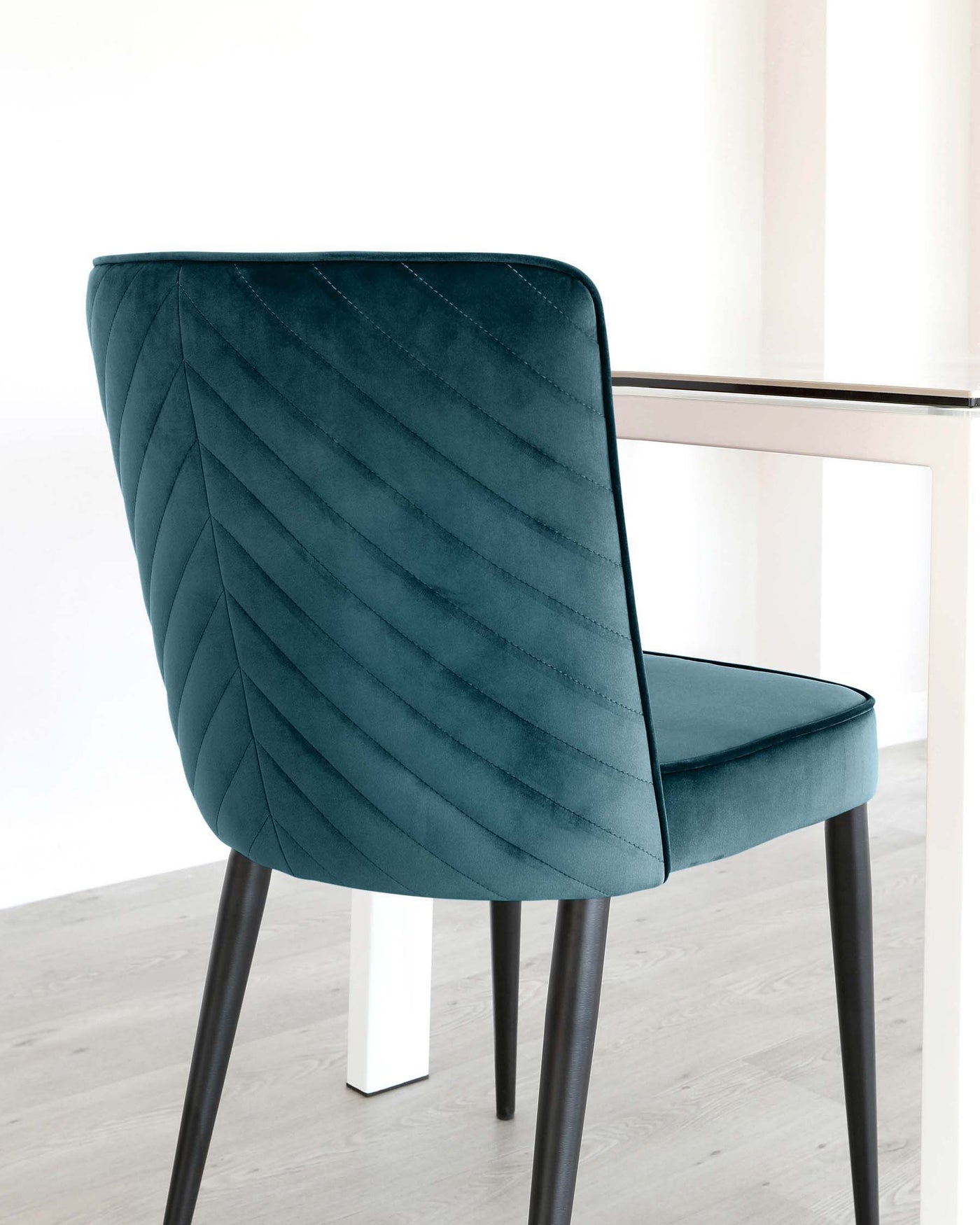 Elegant teal upholstered dining chair with a quilted backrest pattern, featuring black metal legs and a comfortable, curvaceous silhouette.
