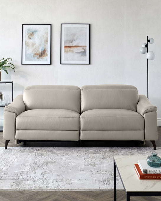 Elegant modern beige leather sofa with clean lines and dark wooden legs, paired with a minimalist black metal side table with a white marble top, placed on a textured off-white area rug.