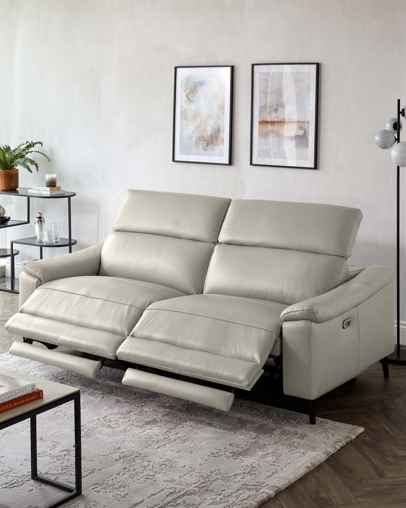Modern light grey leather sectional sofa with reclining footrests, featuring sleek lines and a minimalist design. A slim black metal and glass side table is positioned adjacent to it.