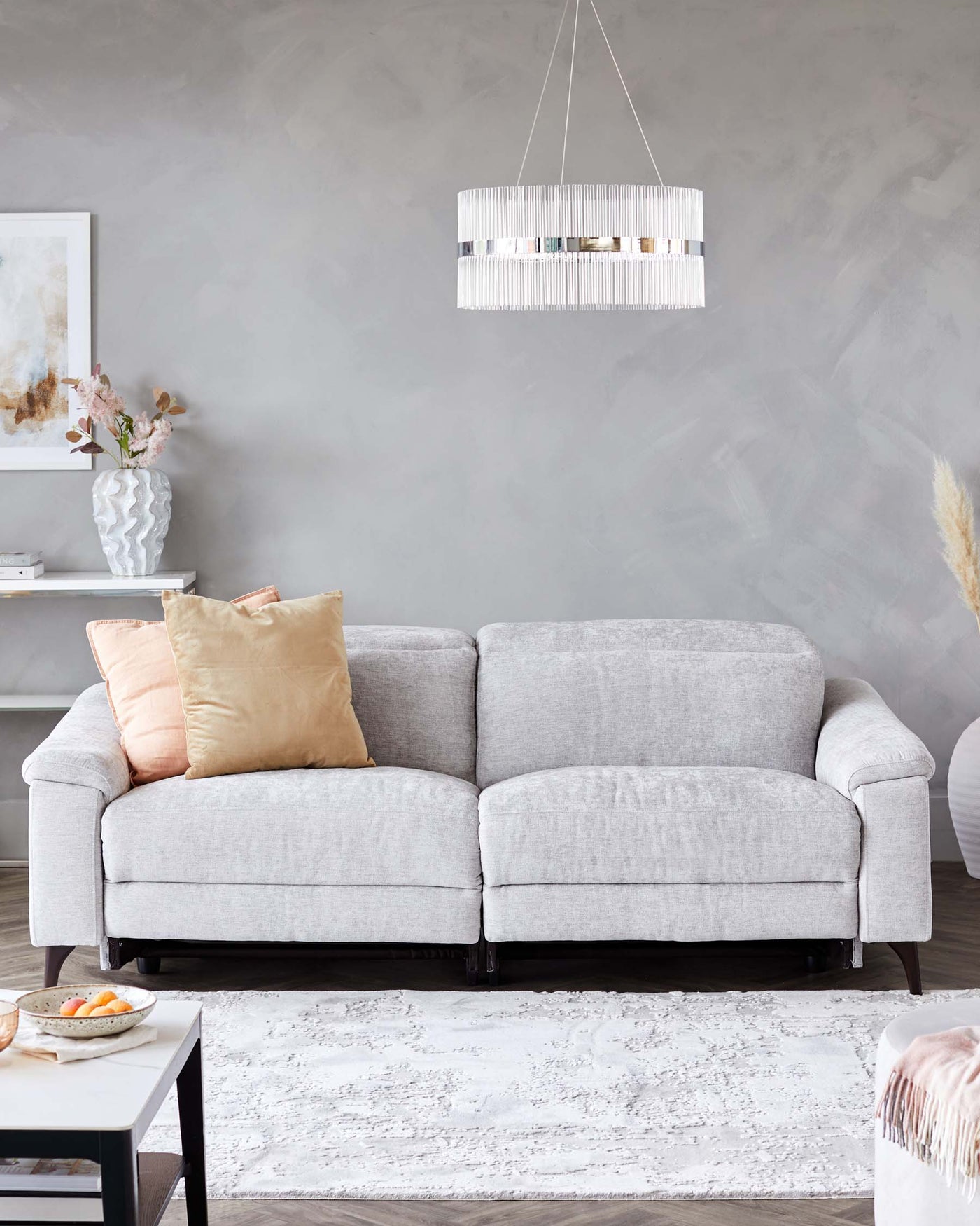 Modern light grey fabric L-shaped sectional sofa with plush cushions and wooden legs, paired with a rectangular white and grey patterned area rug, in a contemporary living room setting. A small white side table with a decorative vase is partially visible.