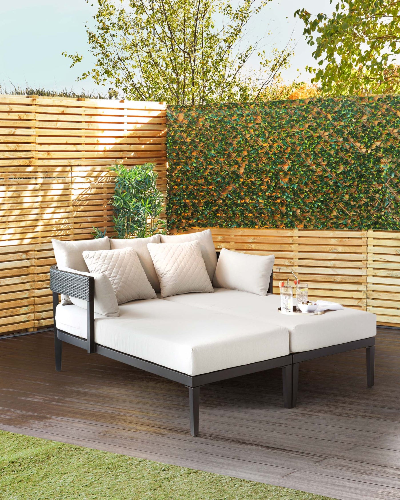 Outdoor corner lounge sofa with a modern aluminium frame, deep cushioned seats, and backrest pillows, set on a wooden deck with greenery in the background.