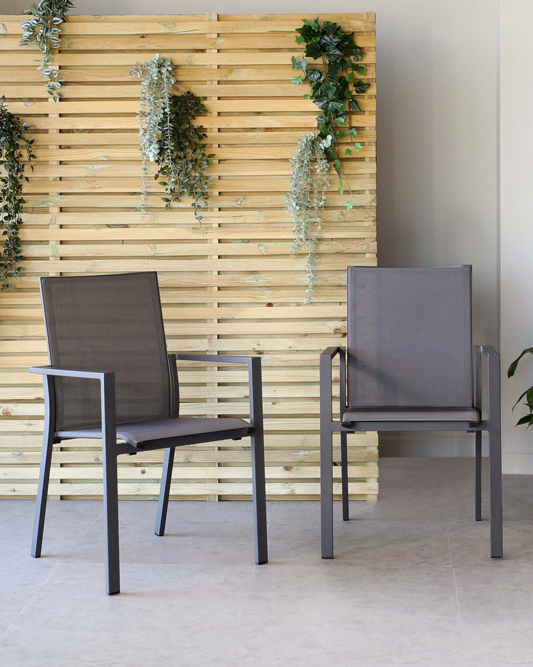 Two modern outdoor chairs with sleek metal frames and breathable mesh fabric for the seat and backrest, standing on a tiled floor against a decorative wood slat wall with hanging greenery.