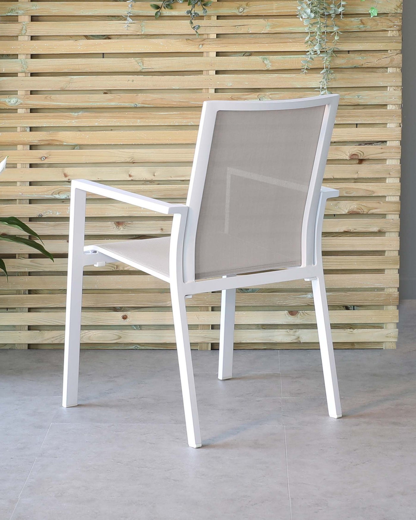 Modern outdoor chair featuring a white aluminium frame with sleek straight lines and a grey sling fabric for the seat and backrest, positioned against a wooden slat wall with greenery accents.