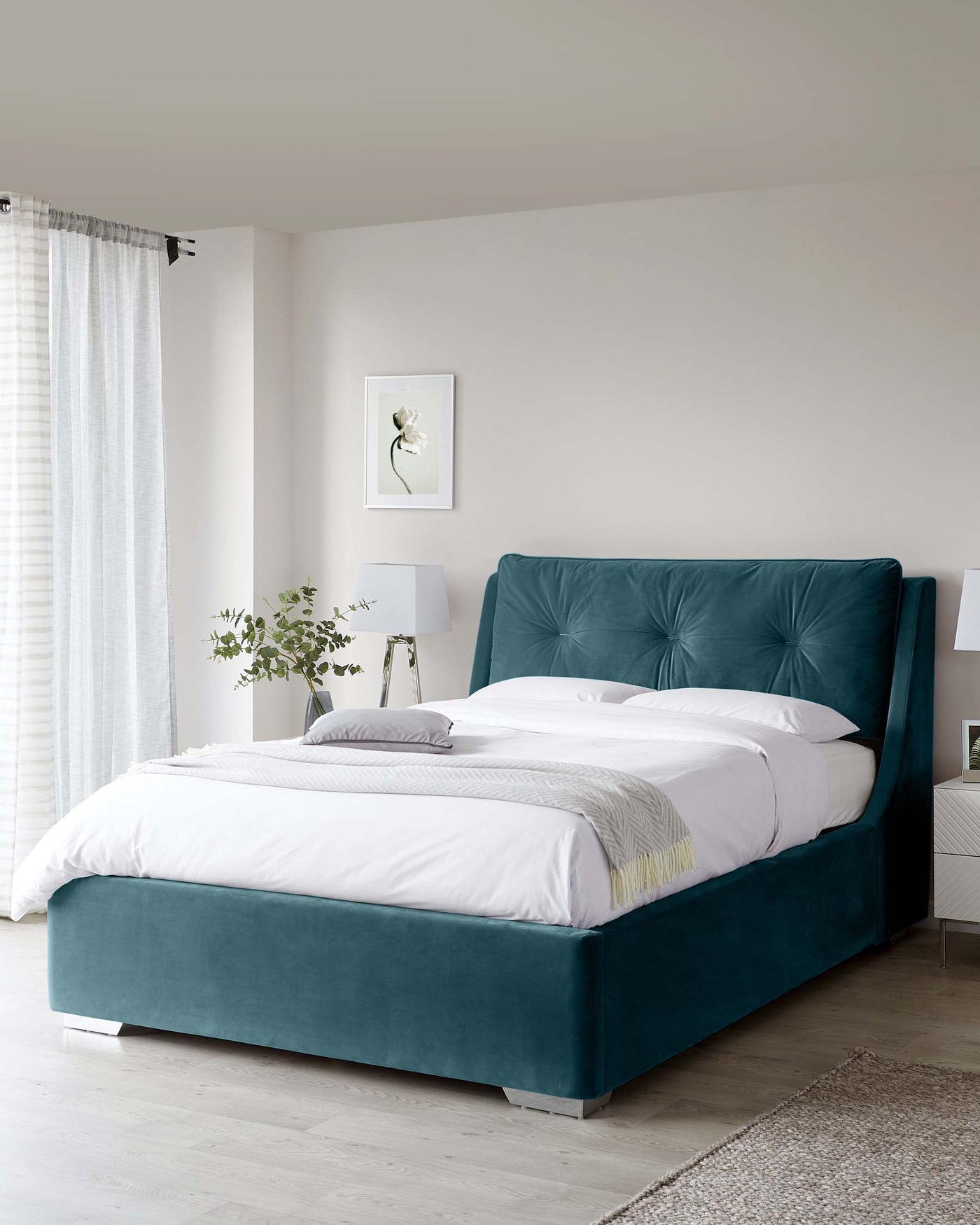 Elegant teal upholstered bed with a tufted headboard and a matching bed base, featuring crisp white bedding and a light throw blanket with a white nightstand and modern lamp on the side.