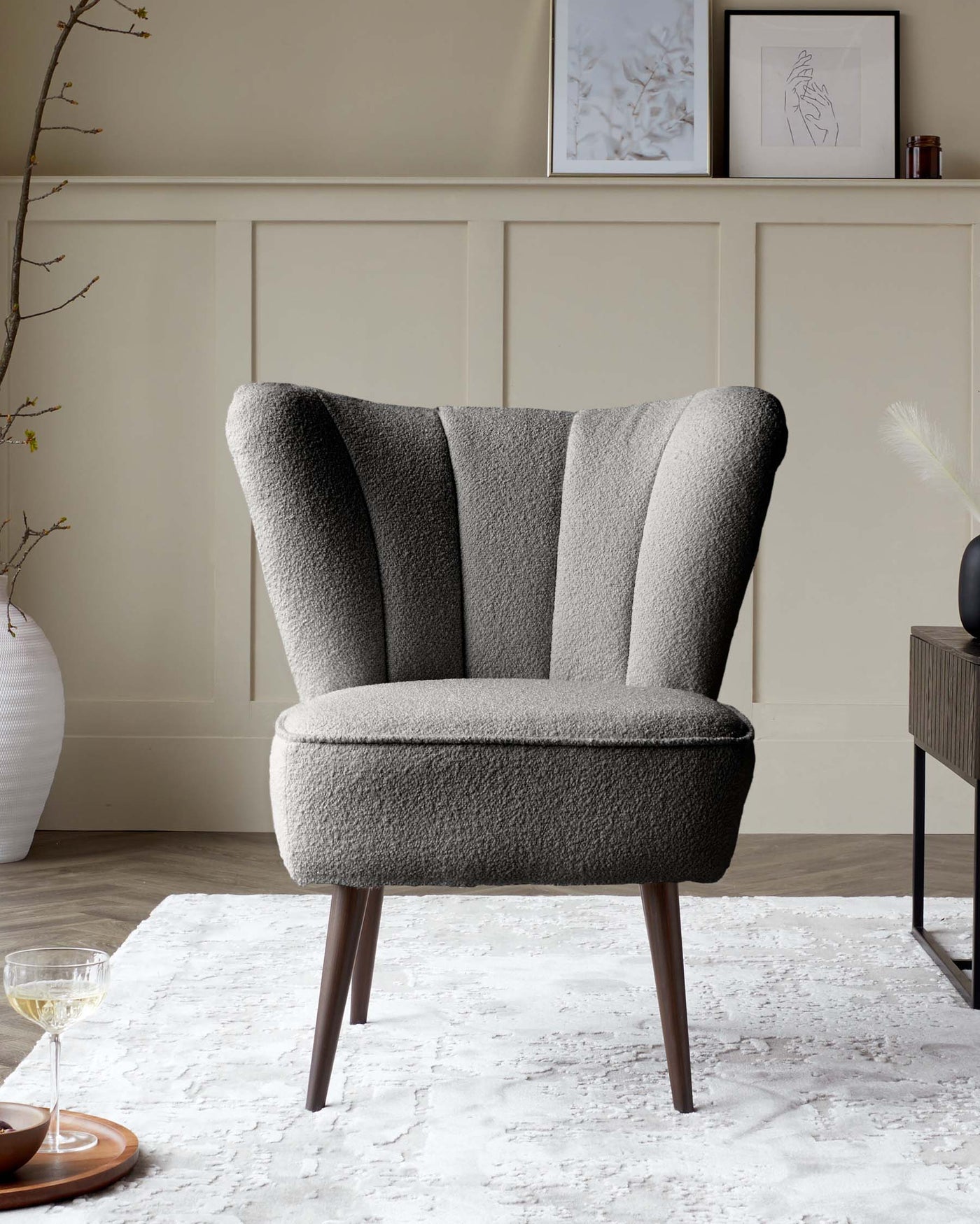A modern textured fabric wingback chair with a high back and curved lines, coloured in shades of grey, with tapered dark wooden legs, situated on a white and grey patterned area rug.