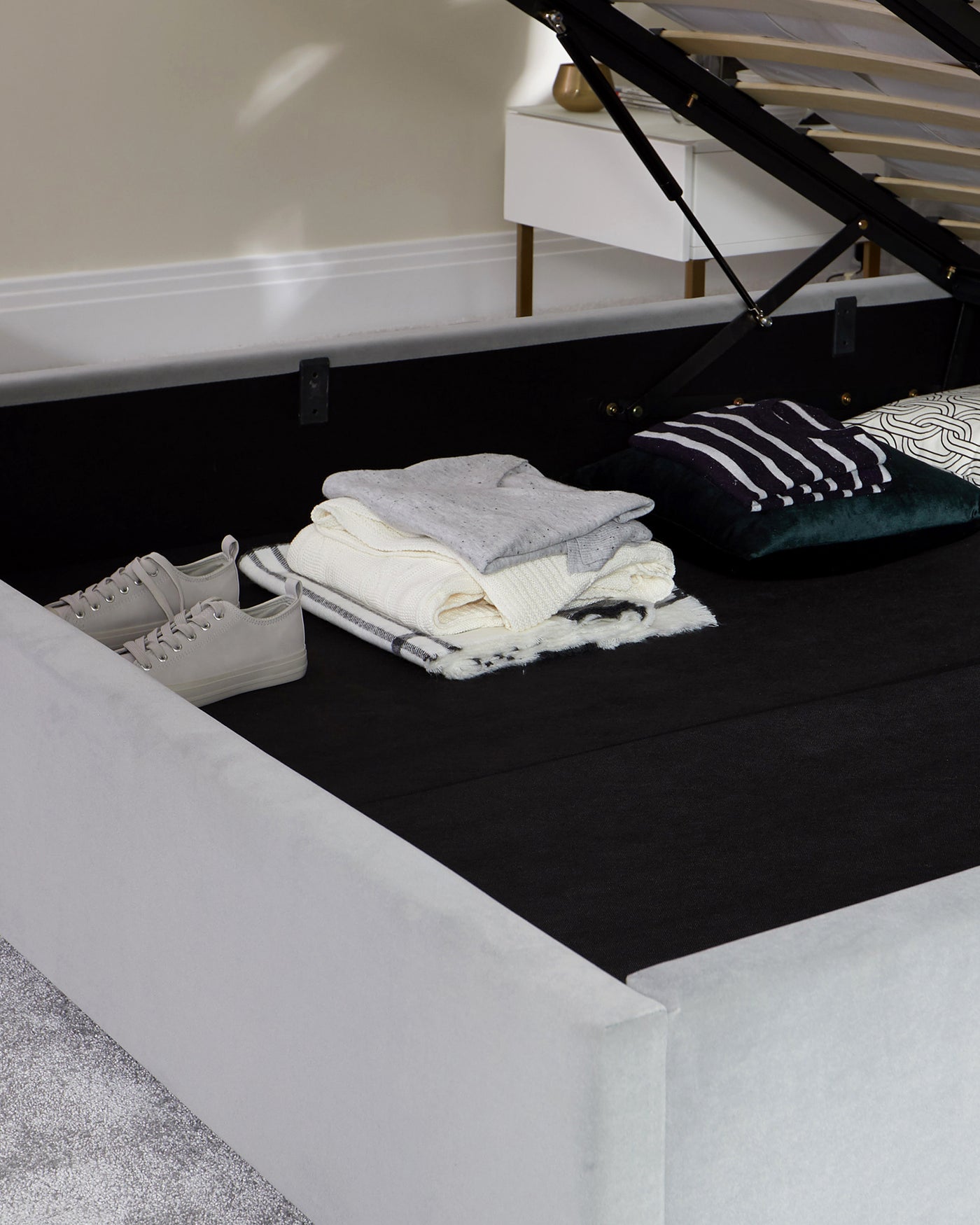 Contemporary grey upholstered ottoman storage bed partially lifted to reveal storage space, with black interior, supported by slender wooden legs.