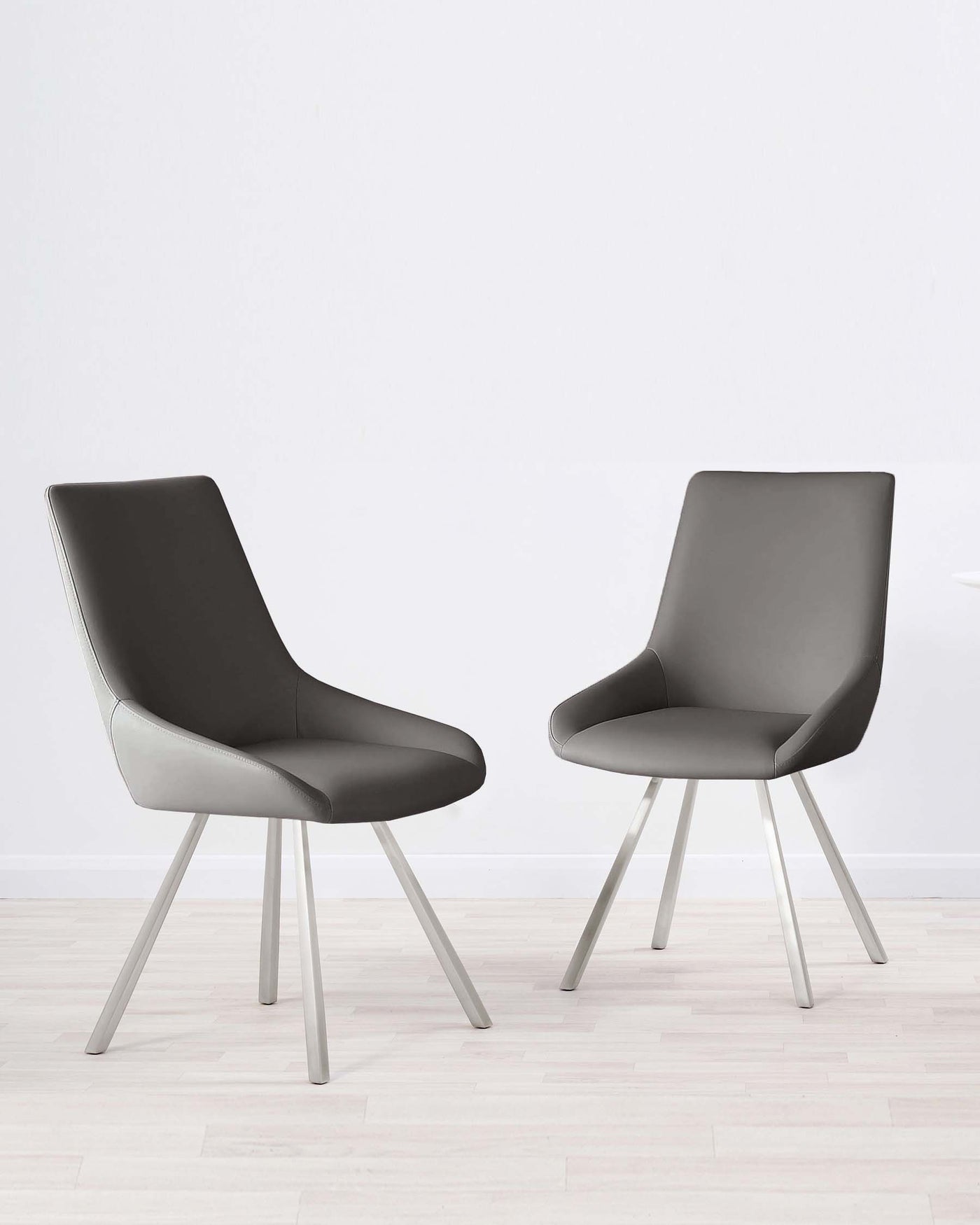 Two modern grey upholstered dining chairs with sleek metal legs, set on a light hardwood floor against a white wall background.