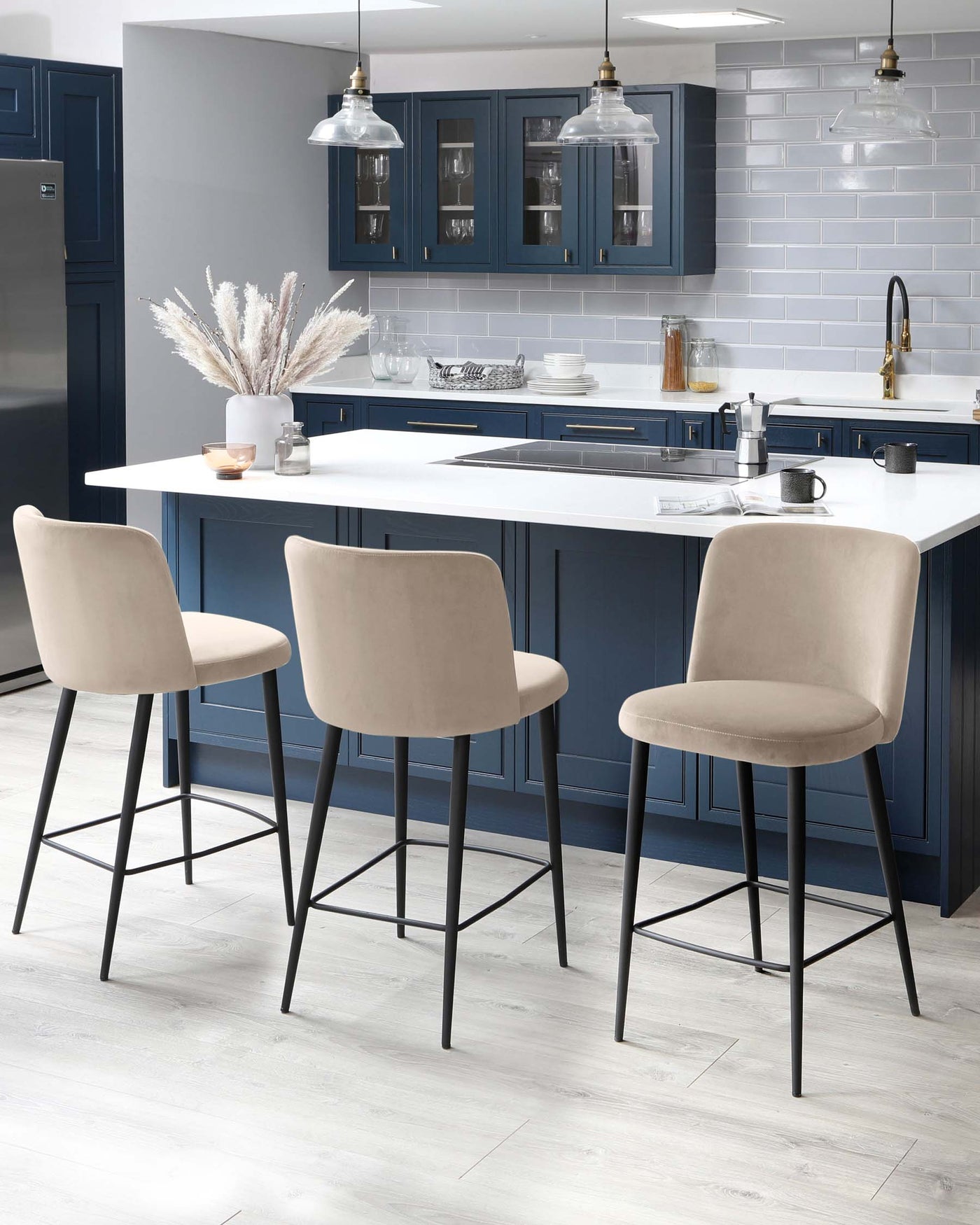 Three modern kitchen bar stools with beige upholstery and black metal legs, featuring a minimalist design and a simple footrest.