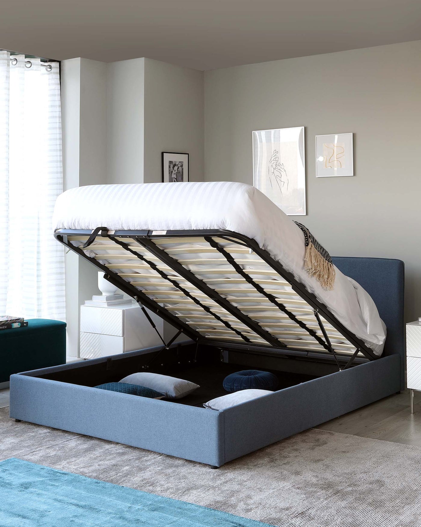 Modern upholstered platform bed with an easy-lift hydraulic system revealing under-bed storage, supported by a slatted base, set in a cosy bedroom with minimalist decor.
