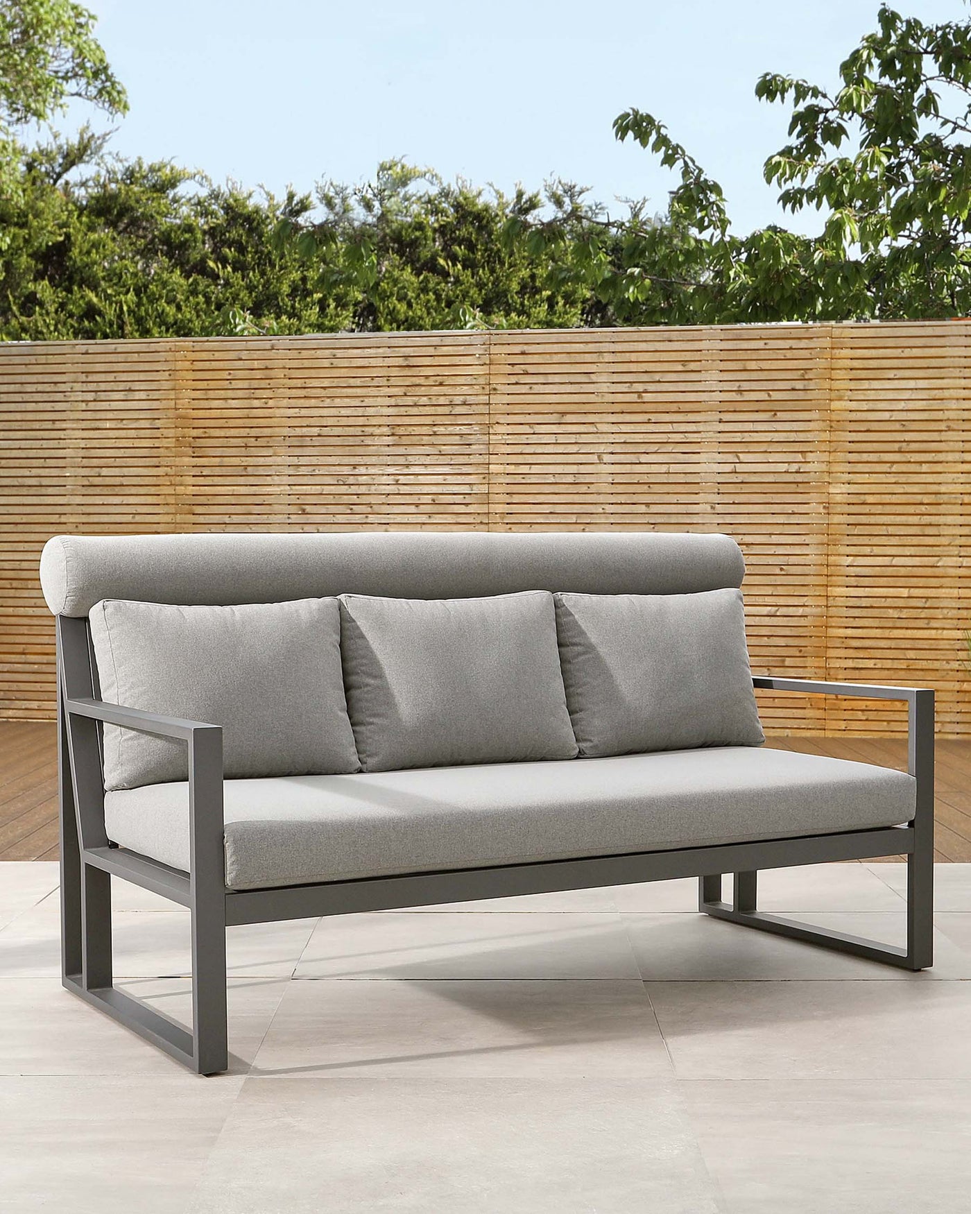 Modern outdoor sofa with a sleek grey metal frame and light grey cushions, featuring clean lines and minimalist design, set against a natural bamboo backdrop.