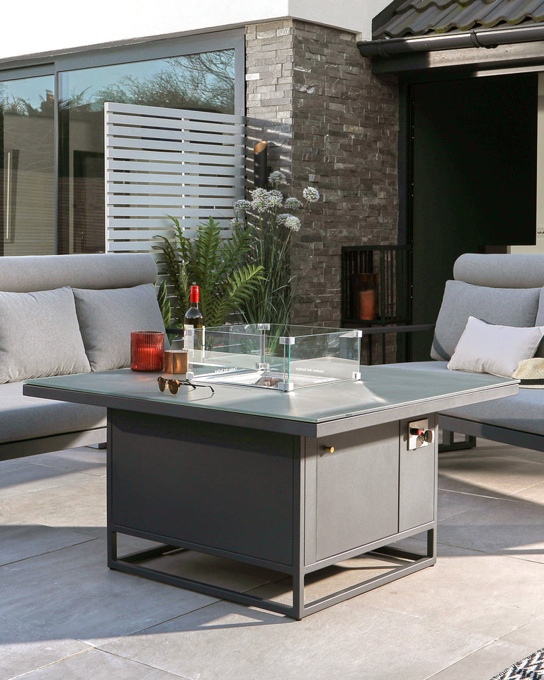 Contemporary outdoor lounge set featuring a grey modular sectional sofa with plush cushions and a square fire pit coffee table with a glass wind guard and a black metal frame.