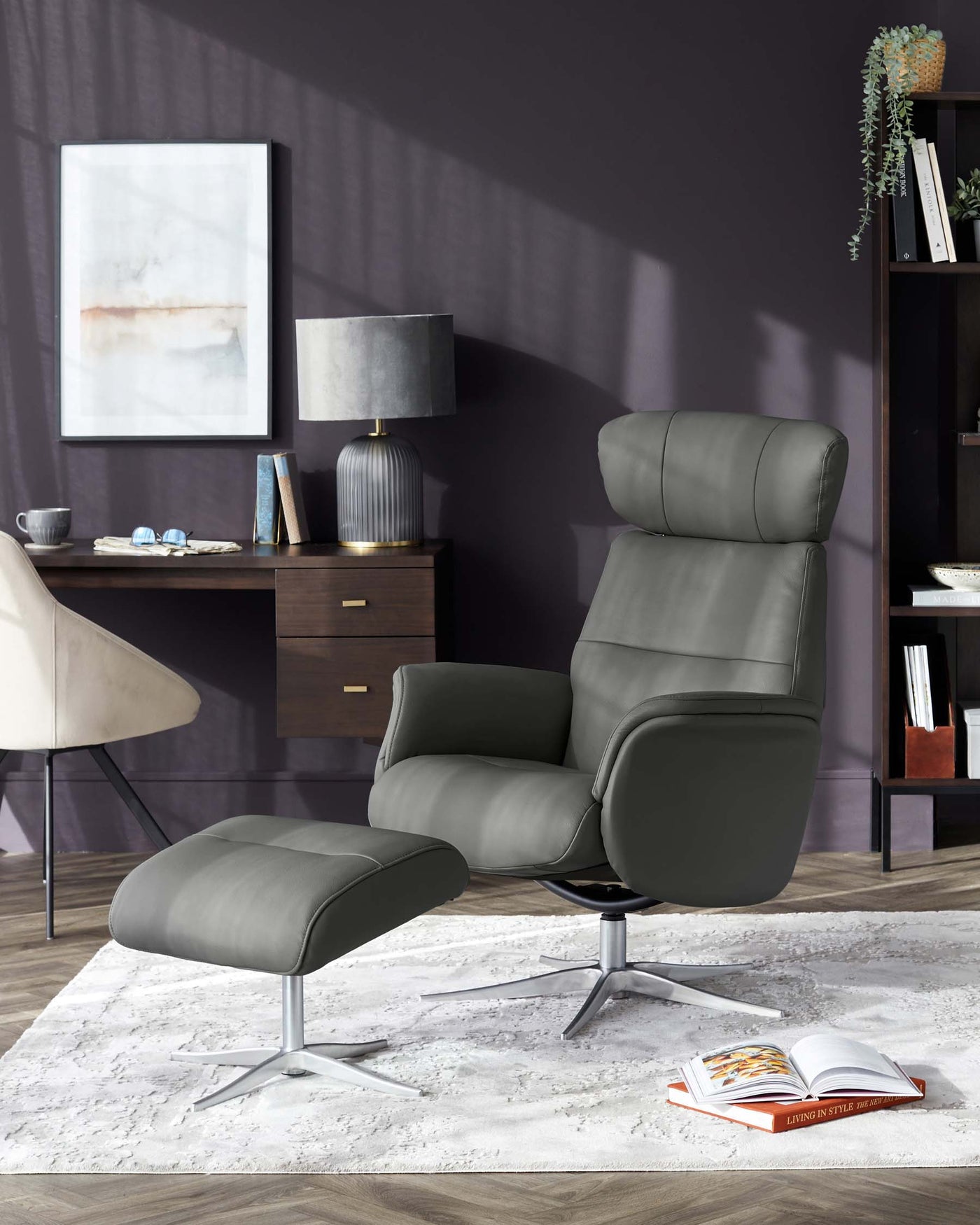 Modern grey leather recliner chair with matching footstool, featuring a sleek metal base, showcased in a contemporary living room setting with a wooden sideboard and shelving unit in the background.