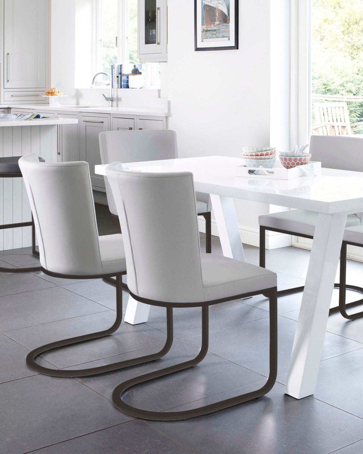 A modern dining set featuring a white rectangular table with a glossy finish and sturdy square legs, paired with three light grey cantilever dining chairs that have high backs and are upholstered for comfort. The chairs' unique base design in a dark metallic finish provides a sleek, floating appearance. The setting is a bright dining room with natural light.