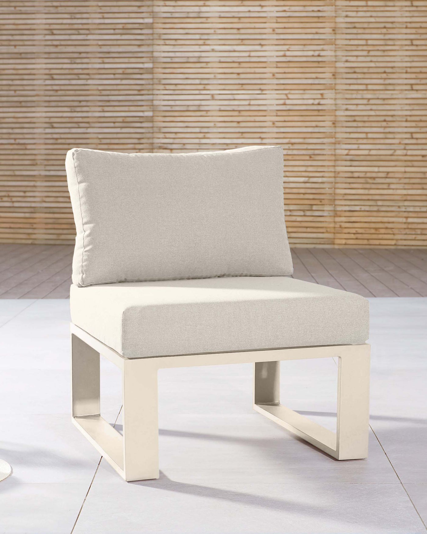 Modern minimalist armless chair with a beige upholstered cushion seat and backrest, featuring a sleek, cream-colored metallic base in a rectangular frame design. Set against a backdrop with a textured bamboo wall.